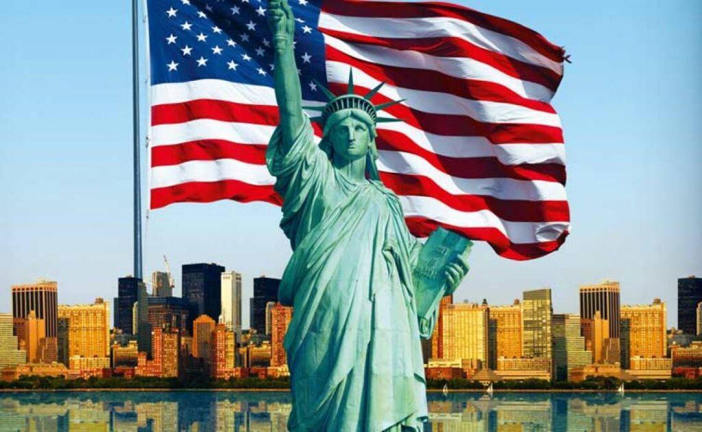 lo sky line di New Yorg con in primo piano la bandiera americana e ka statua della libertà